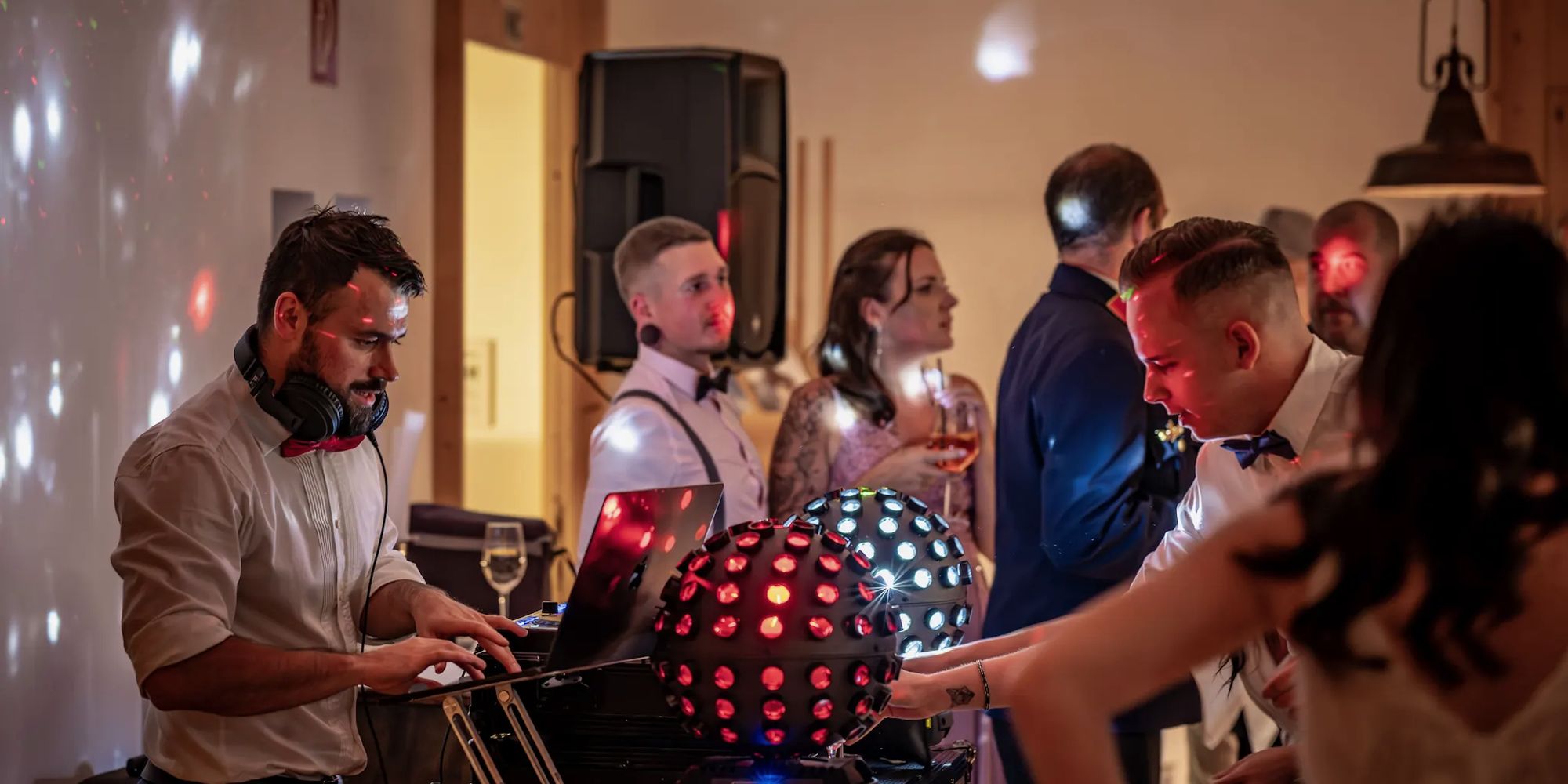 Feiernde Gäste vor dem DJ-Pult, Daniel Wulz mit erhobenen Armen dahinter