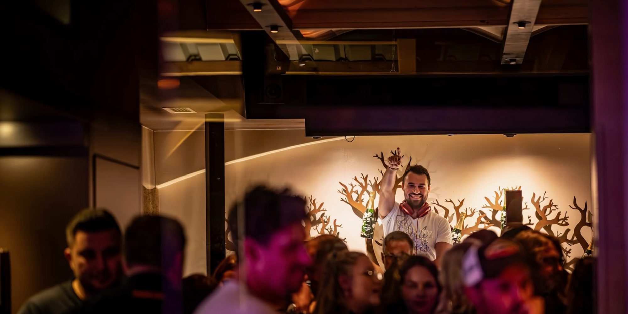 Volle Bar: Gäste im Vordergrund, dahinter DJ Daniel Wulz mit erhobener Hand am Pult