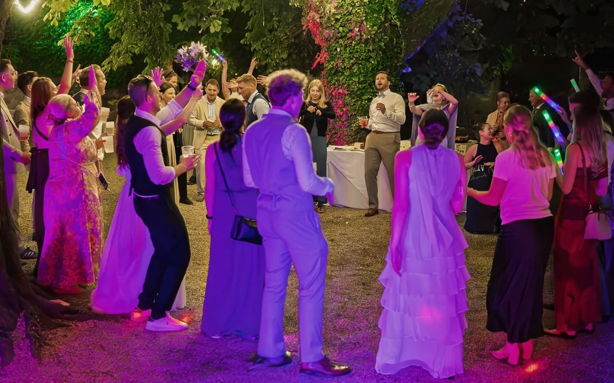 Hochzeitsgäste tanzen abends im Freien unter Lichterketten