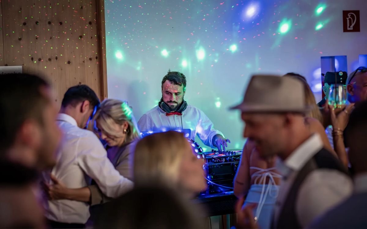 DJ Daniel Wulz am Pult hinter tanzenden Paaren, die Wand dahinter mit grünen und blauen Lichtpunkten